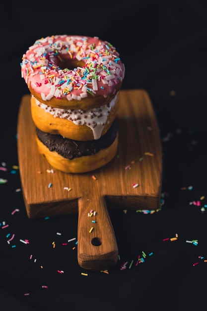 Heerlijke donuts op een houten bord geplaatst op een houten snijplank op zwarte achtergrond