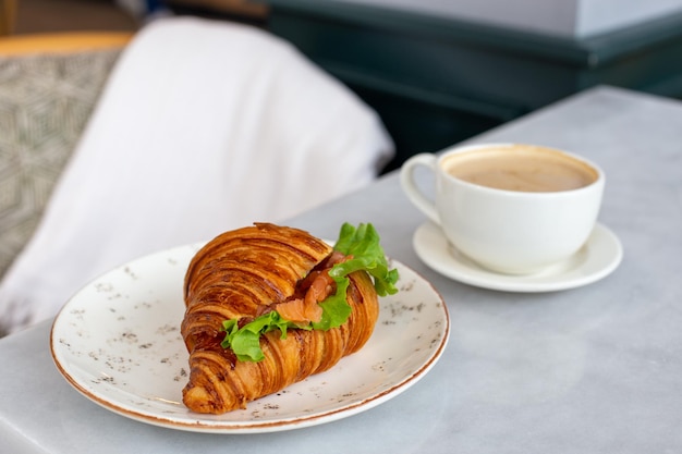 Heerlijke en gezonde ontbijtcroissant met zalmsla en roomkaas op een bord en cappuccinokoffie