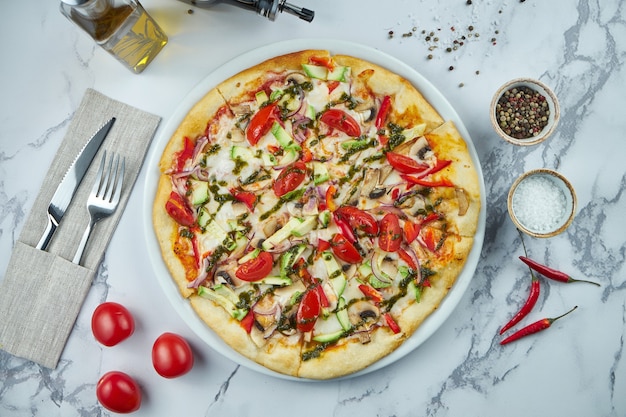 Heerlijke en knapperige Italiaanse vegetarische pizza met tomaten, champignons, uien, courgette en pestosaus in een bord op een marmeren ondergrond