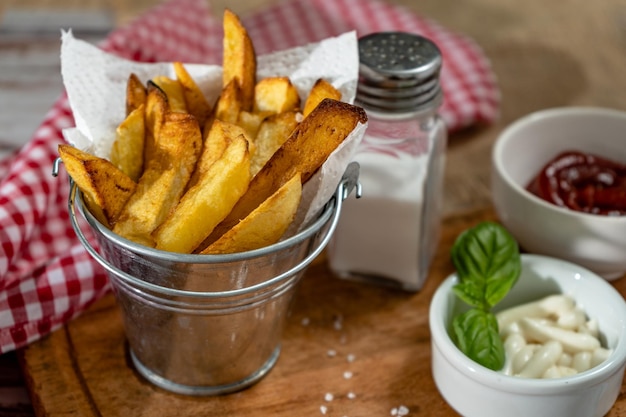 Heerlijke frietjes in een metalen pot met aioli en ketchup op een houten plank