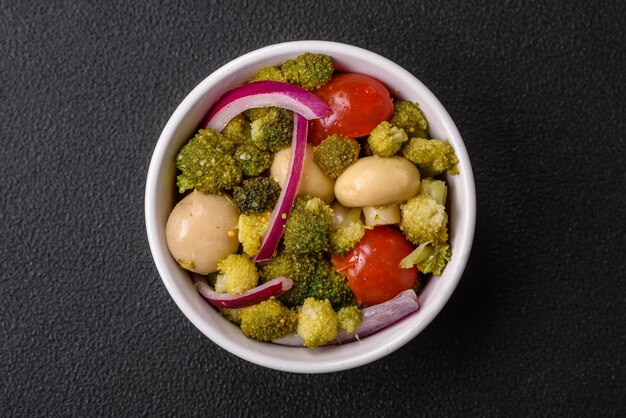 Heerlijke frisse salade met broccoli, kerstomaatjes, champignons, uien, zout, specerijen en kruiden op een donkere betonnen achtergrond