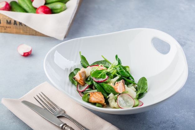 Heerlijke frisse salade met rode vis en groenten. Hete salade met zalm in een witte plaat met bestek op de tafel van een restaurant.