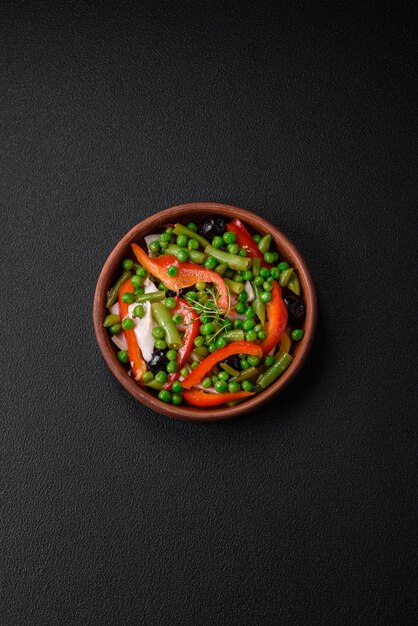 Heerlijke frisse salade van sperziebonen, erwten, paprika en kaas met zout en kruiden op een donkere betonnen achtergrond