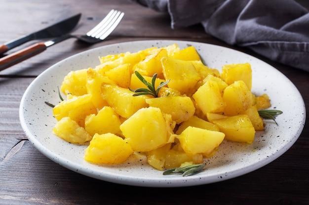 Heerlijke gebakken aardappelen met kruiden kaas en rozemarijn op een bord, een donkere houten tafel.