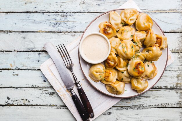 Heerlijke gebakken dumplings met saus op een witte plaat over houten achtergrond bovenaanzicht