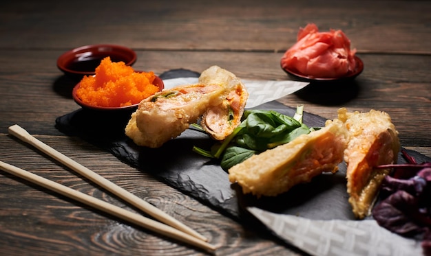 Heerlijke gebakken sushi rollen met rijst en vis op zwarte leisteen geserveerd op de houten tafel versierd met stokjes kom sojasaus kaviaar en spruiten en gember