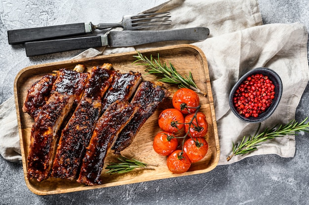 Heerlijke gegrilde spareribs gekruid met een pittige rijgsaus en geserveerd met gebakken tomaten. Grijze achtergrond. Bovenaanzicht