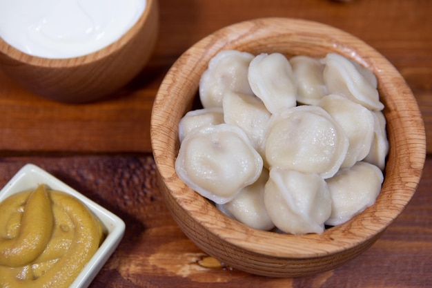 Heerlijke gekookte dumplings op een houten ondergrond met mosterdsaus, zure room en brood