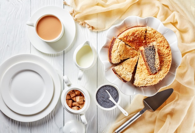 Heerlijke gesneden poppy seed crumble cheesecake op een witte schotel geserveerd met een kopje engelse thee met melk op een houten tafel, horizontale weergave van bovenaf