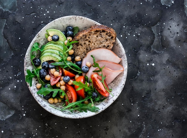 Heerlijke gezonde ontbijtsnack ham en avocado rucola kikkererwten tomaten bosbessen salade op een donkere achtergrond bovenaanzicht