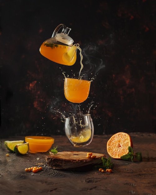 heerlijke gezonde thee met duindoorn in een theepot met sinaasappel en honing gegoten in een glas, op een donkere achtergrond, levitatie