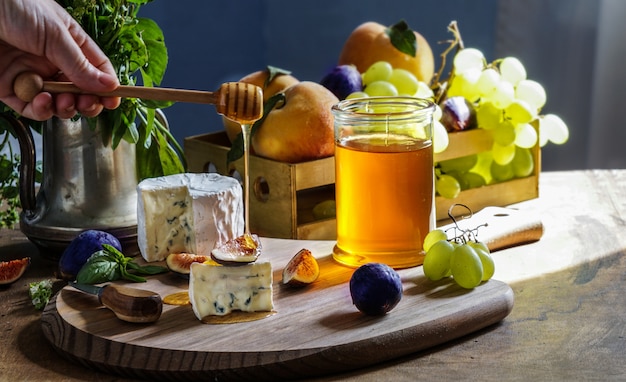 Heerlijke gourmet kaas Dorblu, honing, met gesneden verse vijgen en druiven, perziken, op een rustieke houten tafel