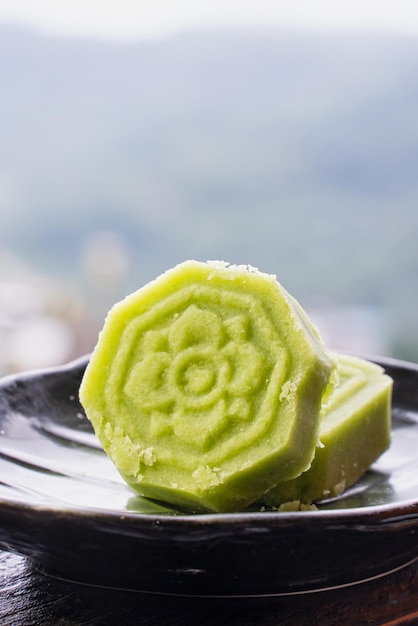 Heerlijke groene mungbooncake met zwarte theeplaat op houten leuning van een theehuis in Taiwan met prachtig landschap op de achtergrond close-up