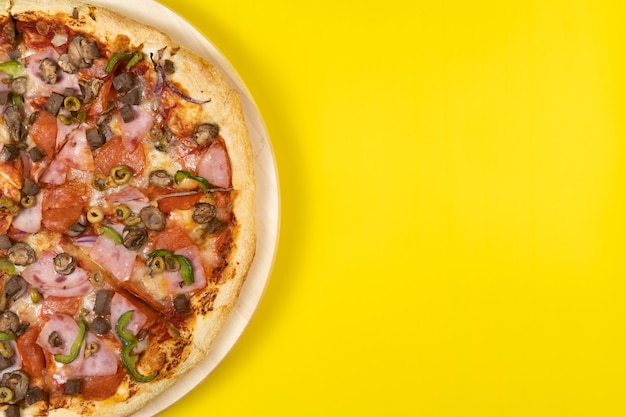 Heerlijke grote pizza met kalfsvlees en champignons op een gele ondergrond.