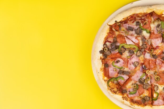 Heerlijke grote pizza met kalfsvlees en champignons op een gele ondergrond.