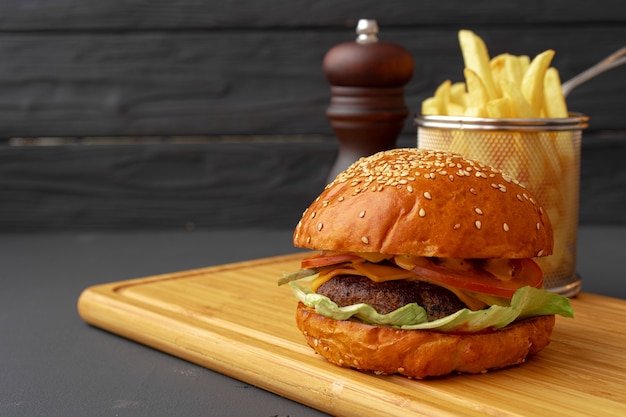 Heerlijke hamburger en frietjes op een houten bord tegen zwarte ondergrond