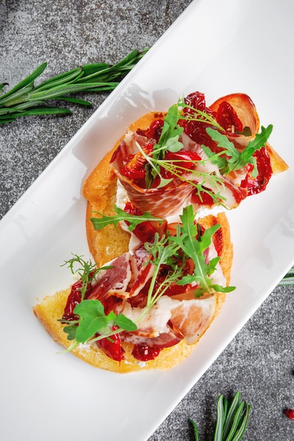 Heerlijke hapjes Bruschetta met spek geroosterde tomaat rode uienringen en rucola Geroosterde croutons met gedroogd vlees en sla