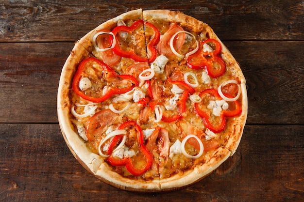 Heerlijke heldere kleurrijke pizza met tomaat, paprika, kip, ham, kaas en ui geserveerd op rustieke houten tafel, plat gelegd. Italiaans fastfood.