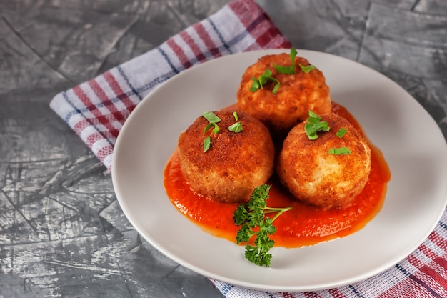 Heerlijke hete Italiaanse arancini - rijstballen gevuld met kaas in tomatensaus, in een plaat op een oude houten tafel