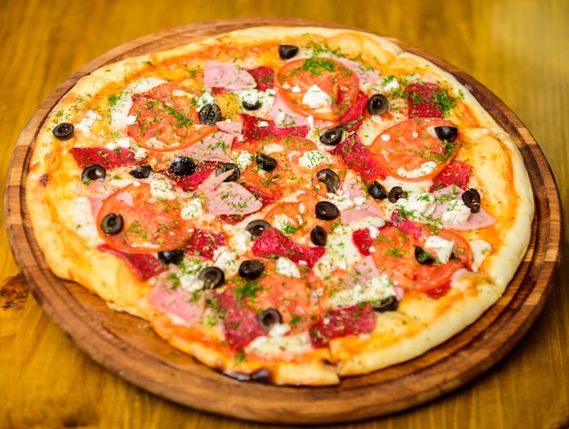 Heerlijke hete pizza op een houten bord. Maaltijdbezorgservice. Pizza met pepperoni, tomaten en zwarte olijven. Haal het voedselconcept weg. Pizzeria-restaurant. Pizza met gehakte dille. Italiaanse pizza.