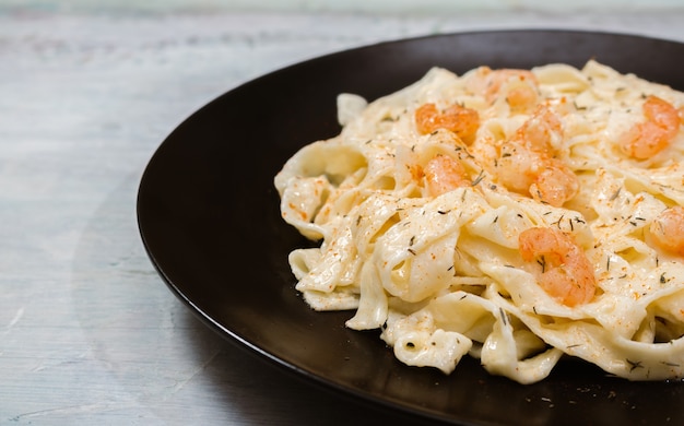 Heerlijke Italiaanse pasta. Fetuccini met garnalen en kruidensaus op zwarte plaat en lichte achtergrond.