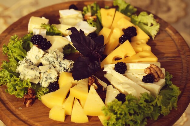 Foto heerlijke kaasplank geserveerd met groene salade, verse basilicum en noten op houten achtergrond