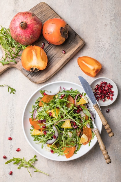 Heerlijke kaki salade met rucola en sinaasappel geserveerd op lichtgrijze tafel, plat leggen. Ruimte voor tekst