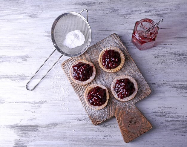 Heerlijke koekjes met jam en poedersuiker op snijplank op houten tafel