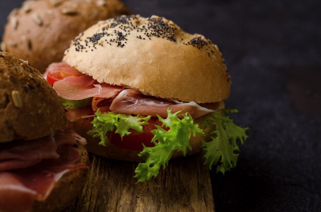 Heerlijke krokante burger bun met gesneden ham op een vintage houten snijplank. Donker humeurig eten stilleven.