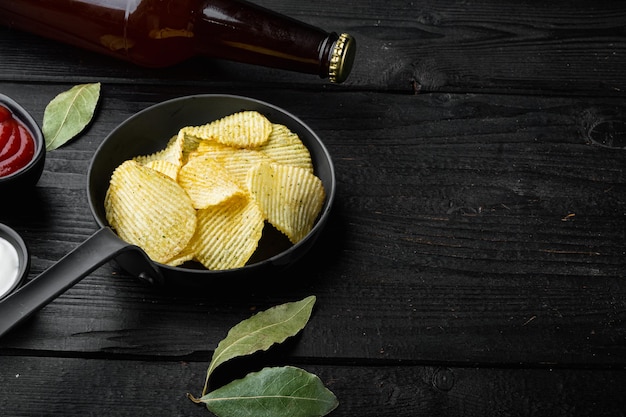 Heerlijke krokante chips en flesje bier op zwarte houten ondergrond met kopieerruimte voor tekst