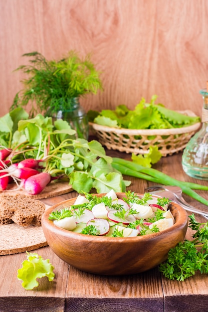 Heerlijke lente groentesalade van komkommer, radijs, kwarteleitjes, kruiden en olie in een bord op een houten tafel
