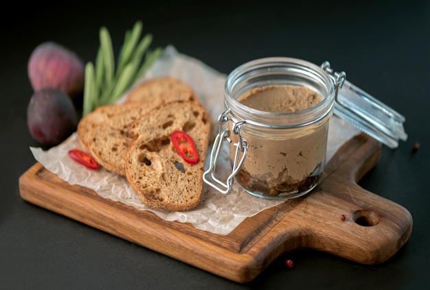 Heerlijke leverpastei met vijgen in een glazen pot en croutons van brood op een zwarte achtergrond