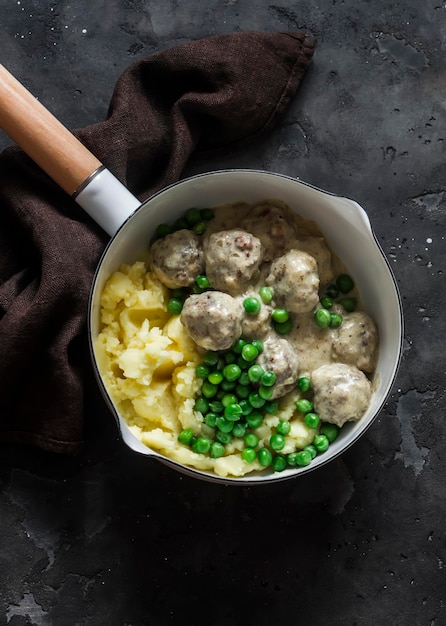 Foto heerlijke lunch aardappelpuree zweedse gehaktballetjes in roomsaus en groene erwten in een pan op een donkere achtergrond bovenaanzicht