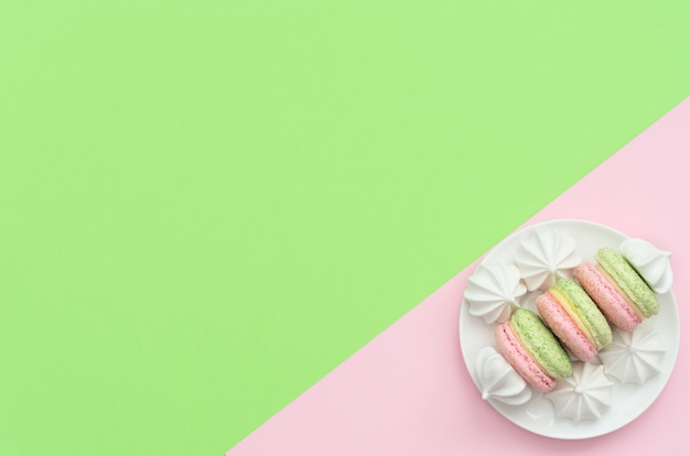 Heerlijke macarons met witte merengues op witte plaat op dubbele groene en roze achtergrond.