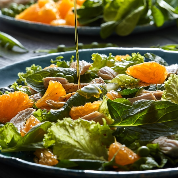 Heerlijke natuurlijke salade met vers geplukte groene groenten, spinazie, groene erwten, sla, oranje fruit, kippenvlees in een blauwe plaat met olijfolie giet in plaat.