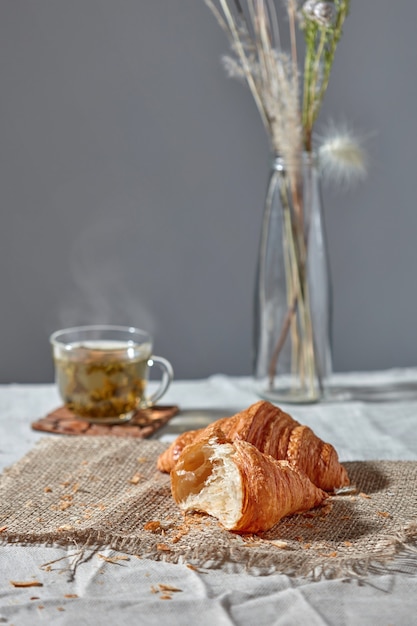 Heerlijke ochtendontbijt met frans zelfgemaakt gebak, kopje groene aromatische verse thee en bloemenvaas op een grijze textielachtergrond. plaats voor tekst.