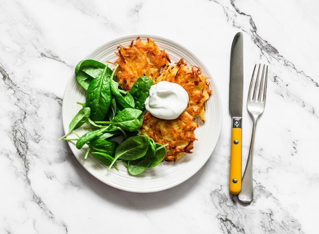 Heerlijke ontbijtaardappelen latkes met zure room en spinaziesalade op een licht bovenaanzicht als achtergrond