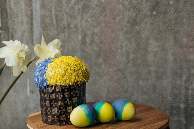 Heerlijke paascake in de kleuren van de vlag van Oekraïne geelblauw gekleurde paaseieren op een houten tafel met bloemen op de achtergrond plaats voor tekst selectieve focus