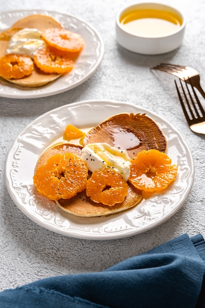 Heerlijke pannenkoeken met mandarijnen en honing of ahornsiroop als ontbijt op een lichte achtergrond.