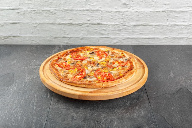 Heerlijke pizza met kip, paddenstoelen, kaas, tomaten en maïs op een betonnen achtergrond.