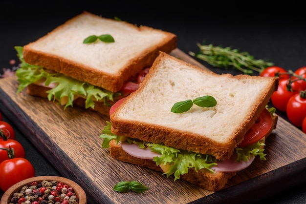 Heerlijke sandwich met toast, ham, tomaten, kaas en sla met zoute specerijen en kruiden op een donkere betonnen achtergrond