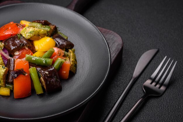 Heerlijke sappige frisse salade van gebakken aubergine-tomaten, courgette-uien, kruiden en zout op een donkere betonnen achtergrond