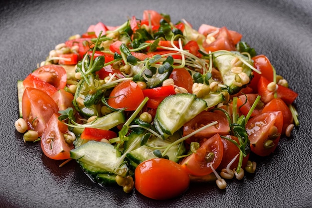 Heerlijke sappige frisse salade van tomaten, paprika's, komkommer, microgreens en gekiemde mungboon op een zwarte keramische plaat op een donkere betonnen achtergrond