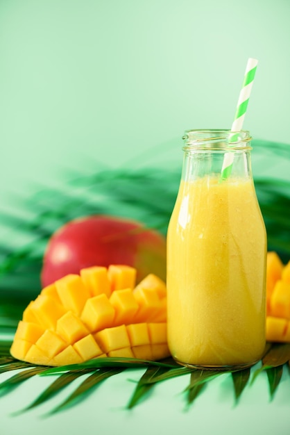 Heerlijke sappige smoothie met oranje fruit en mango op turkooizen achtergrond Kopieer ruimte Popart ontwerp creatief zomerconcept Vers sap in glazen flessen over groene palmbladeren