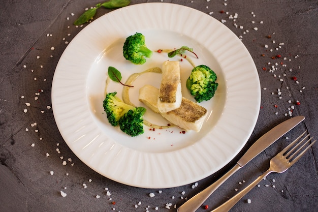 Heerlijke schotel met witte vis en broccoli geserveerd op de witte plaat op de grijze achtergrond. Restaurant menu.