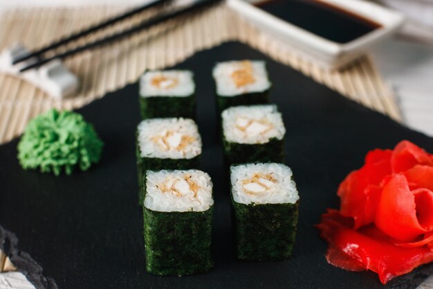 Heerlijke, smaakvolle en verse sushi rolls geserveerd op zwarte leisteen met gember en wasabi. Set van Japanse maki met zalmtartaar verpakt in nori, close-up.