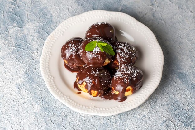 Heerlijke soesjes met chocolade en wit bord. Selectief focusbeeld op lichte achtergrond.