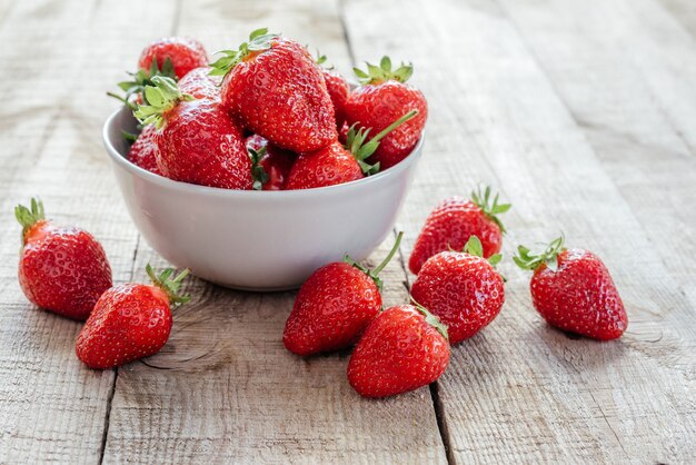 Heerlijke stawberries in een kom op houten tafel met groene bokeh achtergrond, zomerfruit en vitaminen