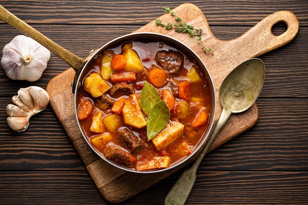 Heerlijke stoofpot met vlees, aardappelen, wortel en jus in oude rustieke koperen pot op bruine houten achtergrond van bovenaf. Traditionele winter- en herfstschotel ragout met rundvlees en groenten in kookpot