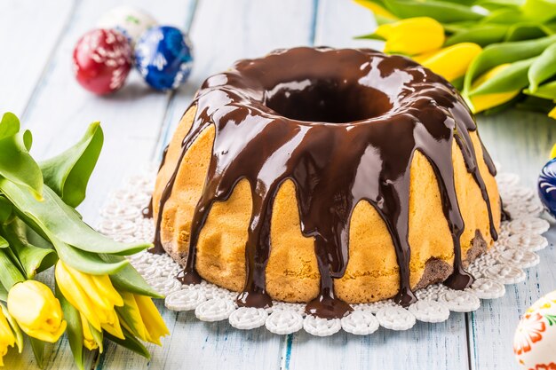 Heerlijke vakantie Slowaakse en Tsjechische cake babovka met chocoladeglazuur. Paasversieringen - lentetulpen en eieren.